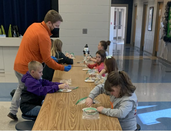 an adult provides kids with snacks while sitting at a table