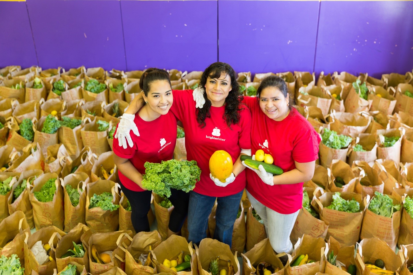 three women stand among a bunch of produce filled bags