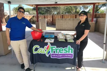 Two people stand next to a table with the CalFresh logo