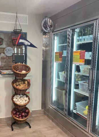 Baskets of onions, potatos and garlic on display next to a food pantry wall refrigeration unit