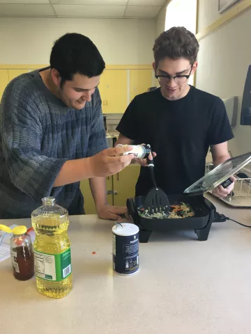 two teens cook together using an electric skillet